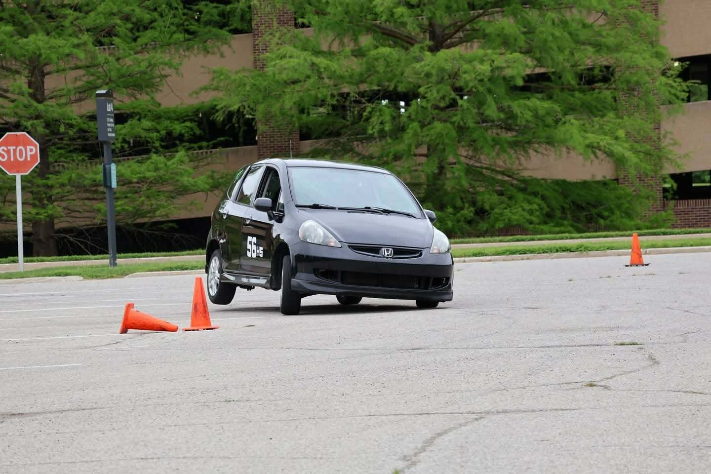 Fit Black Honda Fit number 56HS navigating an orange cone course at an SCCA autocross event in a parking lot